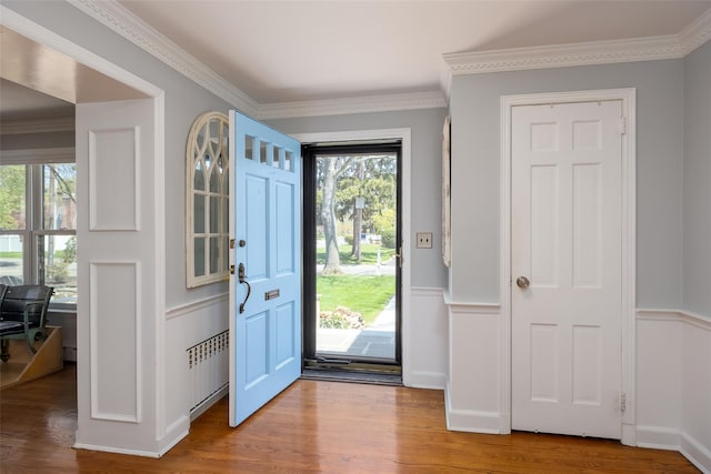 foyer entrance with radiator, wainscoting, ornamental molding, and wood finished floors