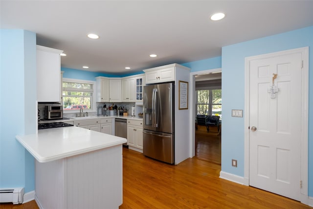 kitchen with white cabinets, stainless steel appliances, light countertops, a baseboard heating unit, and a peninsula