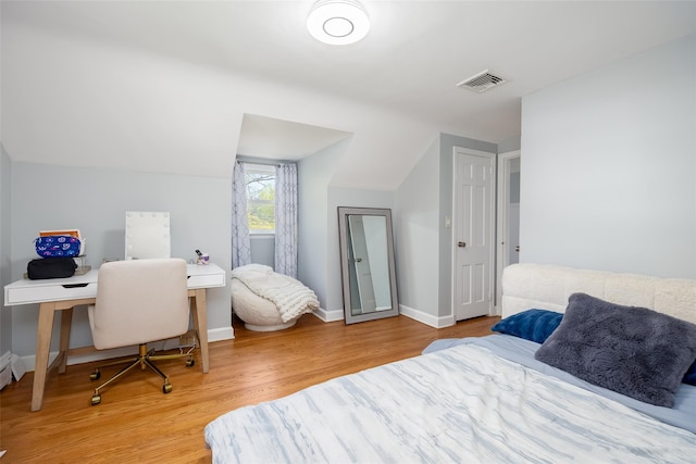 bedroom featuring baseboards, visible vents, wood finished floors, and vaulted ceiling