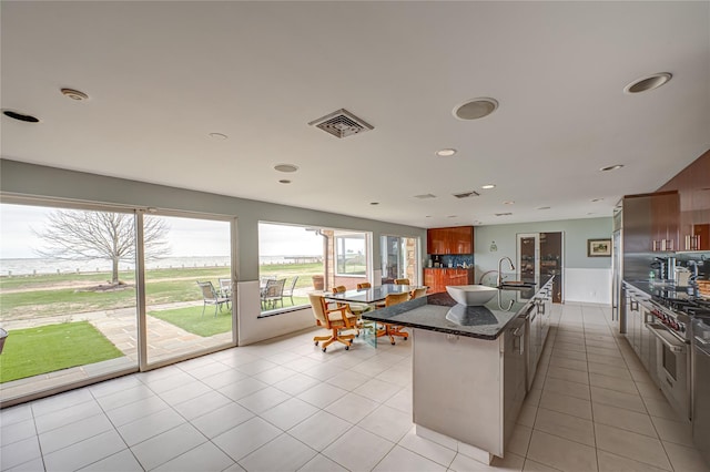 kitchen featuring light tile patterned flooring, a sink, a kitchen island with sink, dark stone countertops, and high end range