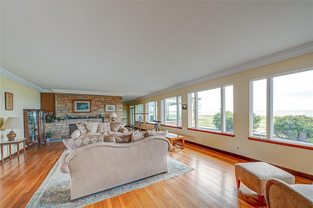 living area with baseboards, ornamental molding, light wood-style flooring, and a stone fireplace