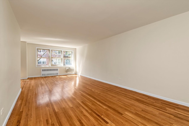 spare room featuring baseboards, light wood-style flooring, radiator, and a wall unit AC
