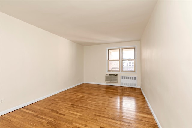spare room with light wood-style floors, radiator, baseboards, and an AC wall unit