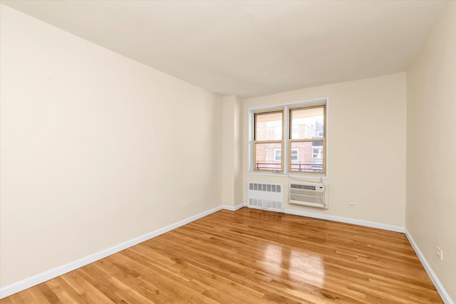 spare room featuring light wood-style floors, radiator, baseboards, and a wall unit AC
