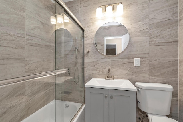 bathroom featuring vanity, enclosed tub / shower combo, toilet, and tile walls