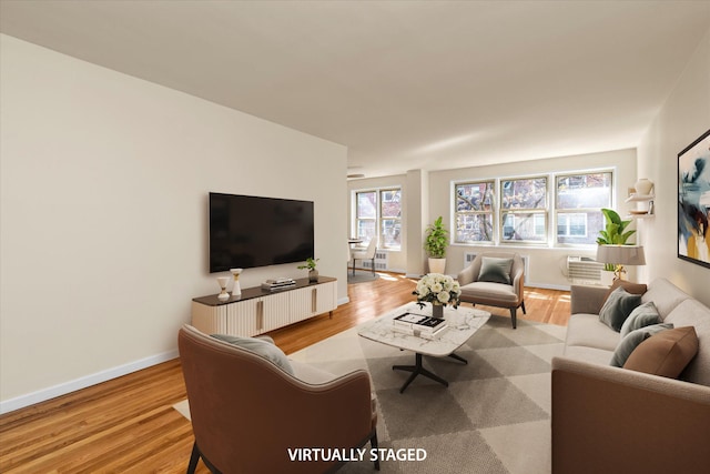 living area with baseboards, light wood-type flooring, and a wall mounted air conditioner