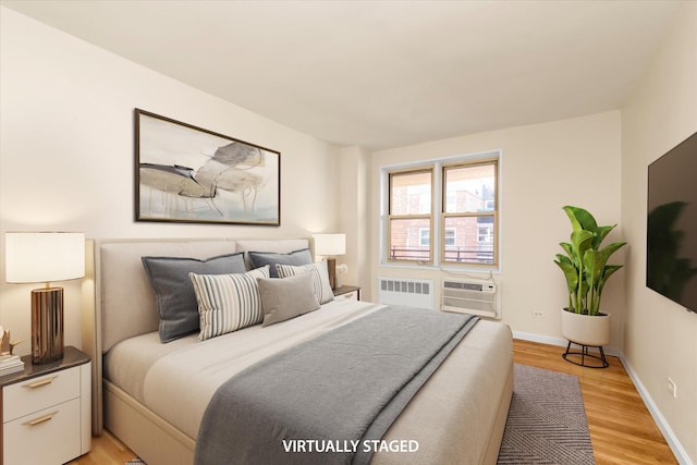 bedroom with radiator heating unit, baseboards, an AC wall unit, and light wood finished floors