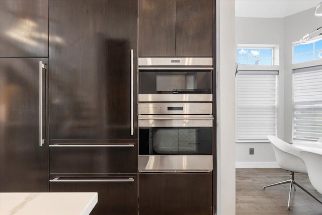 kitchen with wood finished floors, dark brown cabinets, baseboards, high quality fridge, and stainless steel double oven