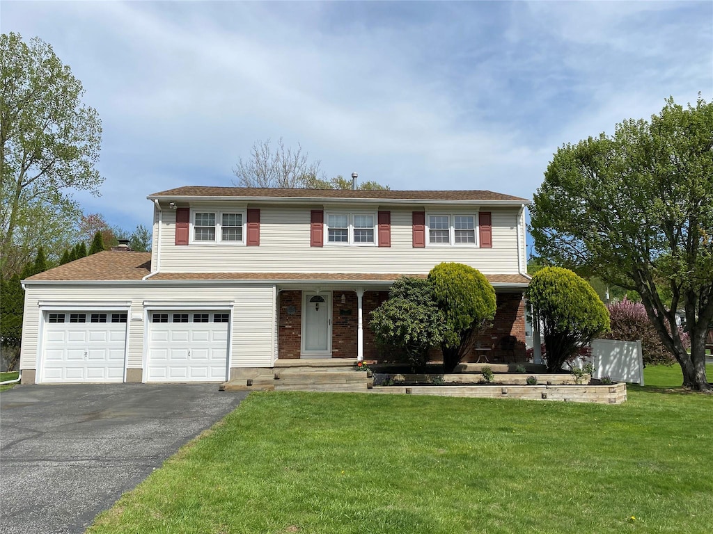 traditional home with an attached garage, aphalt driveway, a front yard, and a porch
