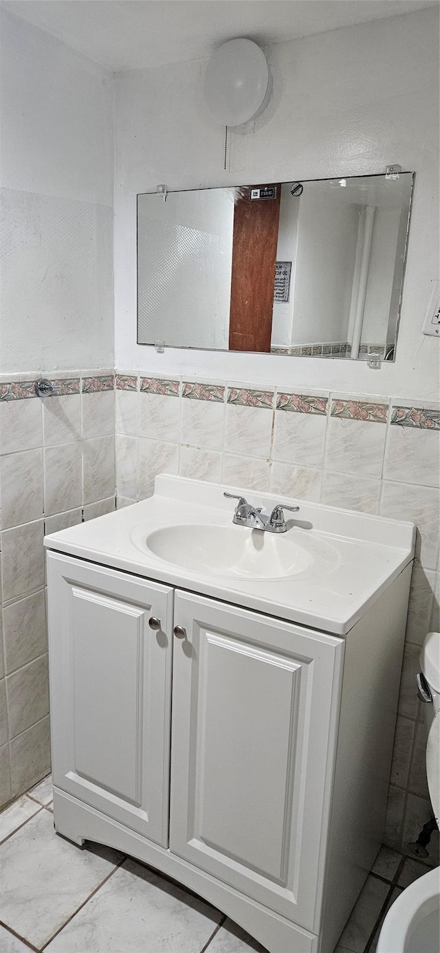 bathroom featuring vanity, toilet, tile walls, a wainscoted wall, and tile patterned floors