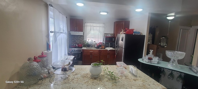 kitchen with decorative backsplash, reddish brown cabinets, recessed lighting, under cabinet range hood, and stainless steel appliances