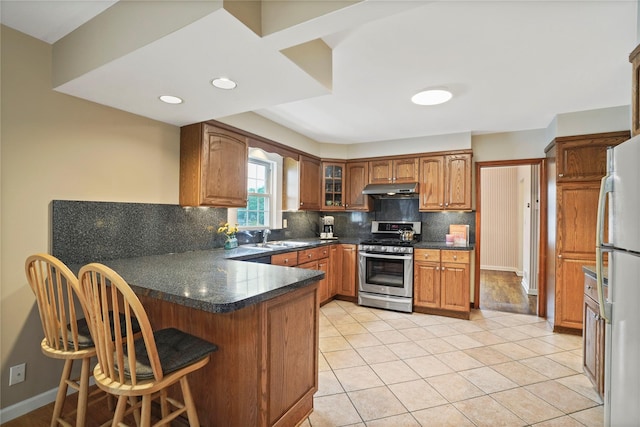 23 Hilldale Rd, Dobbs Ferry, NY 10522 - kitchen featuring stainless steel gas range, under cabinet range hood, freestanding refrigerator, a peninsula, and decorative backsplash