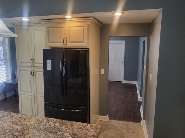 kitchen featuring light tile patterned floors, baseboards, white cabinets, freestanding refrigerator, and light stone counters