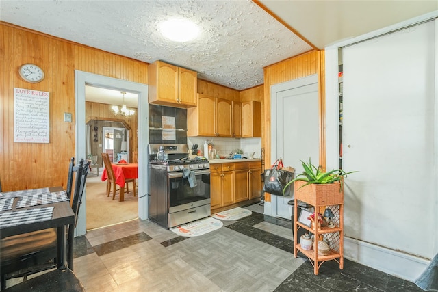 kitchen with wooden walls, an inviting chandelier, stainless steel gas range oven, light countertops, and backsplash