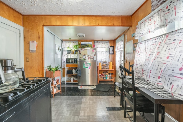 kitchen with wooden walls, a textured ceiling, crown molding, and black appliances