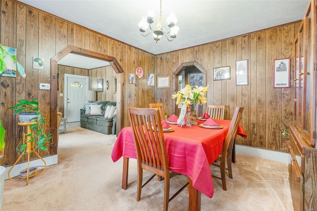 dining area featuring carpet flooring, wooden walls, arched walkways, and a chandelier