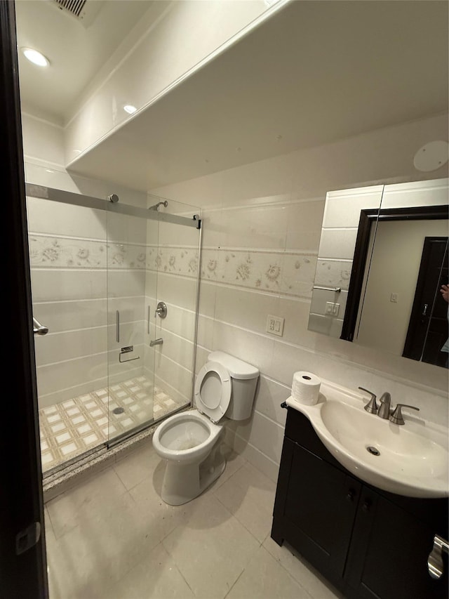 bathroom featuring a stall shower, toilet, tile walls, vanity, and tile patterned flooring