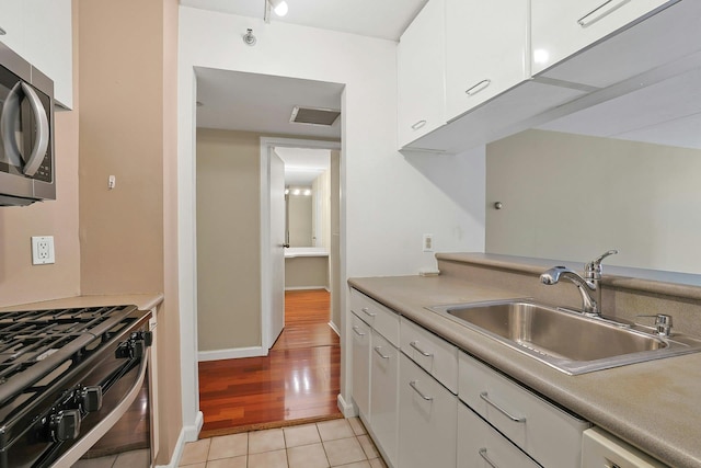 kitchen featuring a sink, white cabinets, stainless steel microwave, light countertops, and gas stove