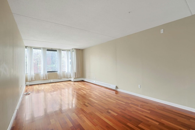 spare room with a baseboard heating unit, baseboards, baseboard heating, and light wood-style floors