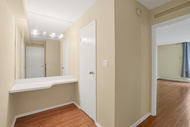 hall with baseboards, baseboard heating, visible vents, and wood finished floors