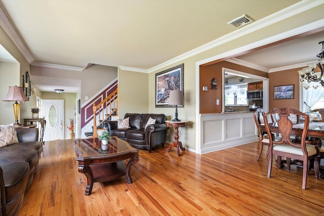 living room with visible vents, light wood-type flooring, stairway, an inviting chandelier, and ornamental molding