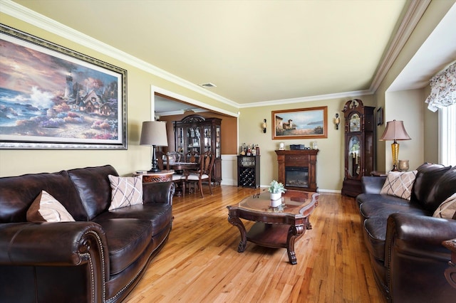 living room featuring visible vents, baseboards, light wood finished floors, a glass covered fireplace, and ornamental molding
