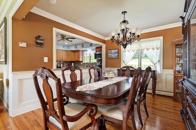 dining space featuring crown molding, a wainscoted wall, light wood finished floors, and a notable chandelier