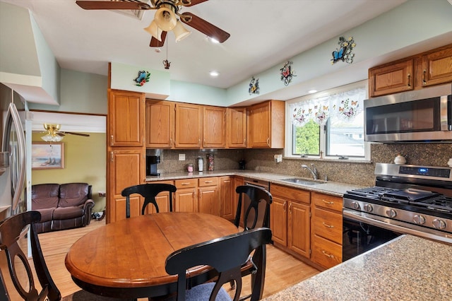 kitchen featuring decorative backsplash, ceiling fan, light wood-type flooring, a sink, and appliances with stainless steel finishes