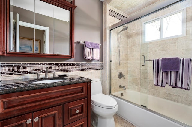 bathroom featuring combined bath / shower with glass door, tile walls, vanity, and toilet