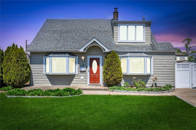 view of front of property featuring a lawn, fence, a chimney, and a shingled roof