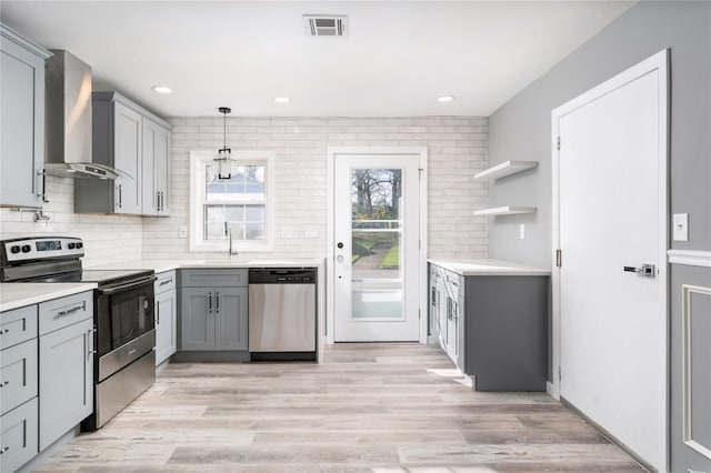 kitchen with gray cabinetry, appliances with stainless steel finishes, wall chimney exhaust hood, and visible vents
