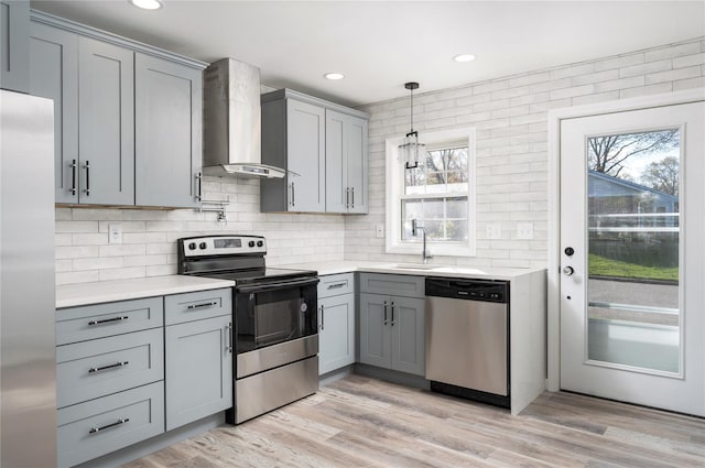 kitchen featuring light countertops, wall chimney exhaust hood, tasteful backsplash, gray cabinetry, and stainless steel appliances