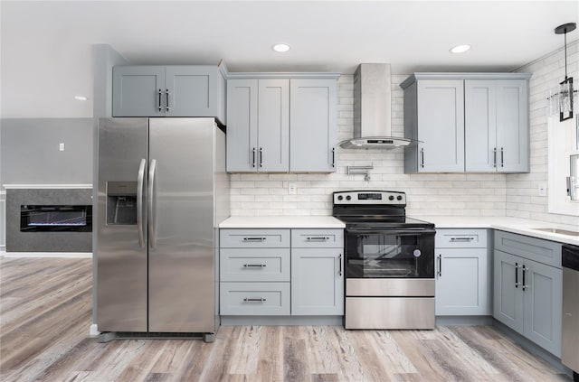 kitchen with decorative backsplash, light countertops, wall chimney exhaust hood, gray cabinetry, and stainless steel appliances
