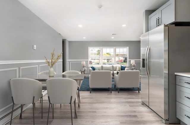 interior space with light wood-style flooring, a decorative wall, a baseboard heating unit, and wainscoting