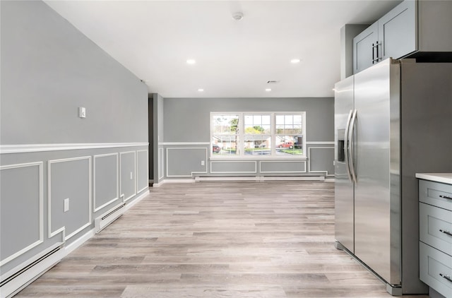 kitchen with stainless steel fridge with ice dispenser, a baseboard radiator, a decorative wall, and light wood-type flooring