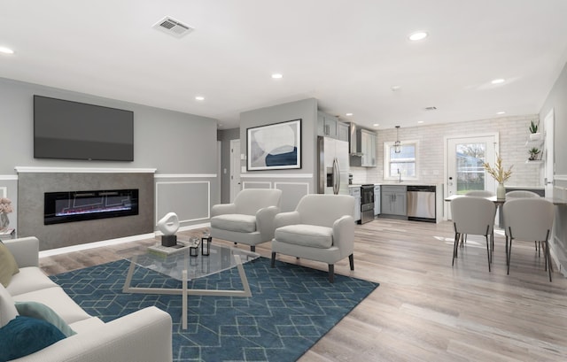 living room with visible vents, recessed lighting, light wood-style flooring, and a glass covered fireplace