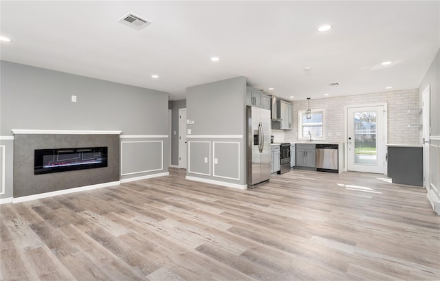 unfurnished living room featuring visible vents, a glass covered fireplace, recessed lighting, a sink, and light wood finished floors