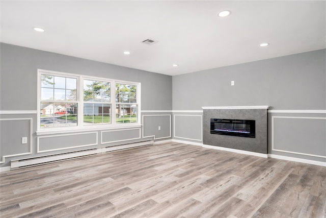 unfurnished living room with visible vents, a baseboard radiator, wood finished floors, and a decorative wall