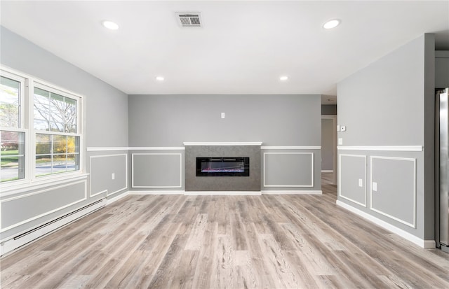 unfurnished living room with visible vents, a baseboard radiator, a glass covered fireplace, light wood-style floors, and a decorative wall