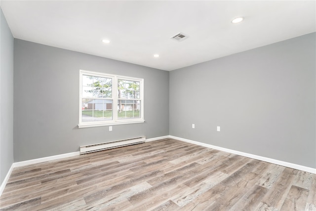 spare room featuring baseboards, a baseboard radiator, light wood-type flooring, and visible vents