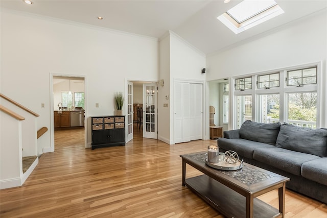 living room with a towering ceiling, a skylight, light wood-type flooring, baseboards, and ornamental molding
