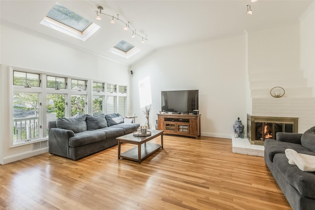 living room featuring a skylight, a fireplace, rail lighting, light wood-type flooring, and high vaulted ceiling