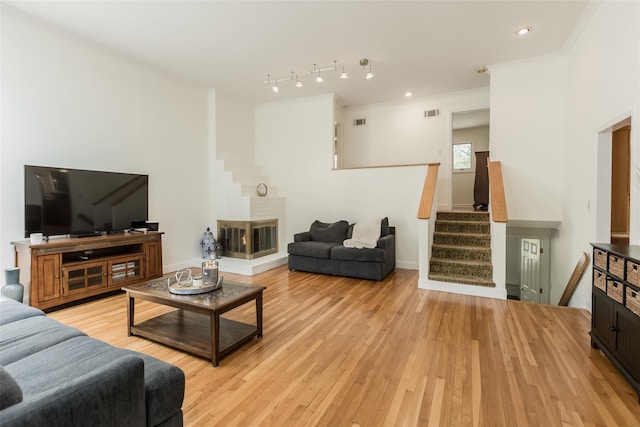 living room featuring stairway, ornamental molding, light wood-style floors, and visible vents