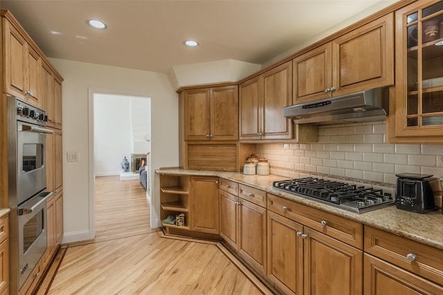 kitchen featuring baseboards, light wood-type flooring, under cabinet range hood, appliances with stainless steel finishes, and backsplash