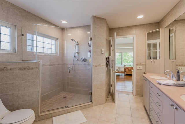 ensuite bathroom with tile walls, tile patterned flooring, a stall shower, a sink, and toilet