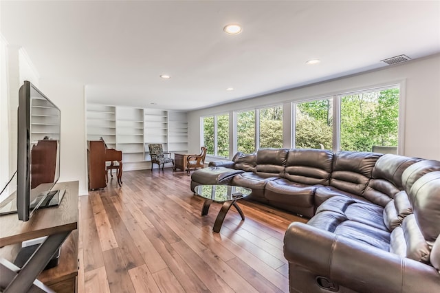 living area featuring visible vents, plenty of natural light, built in shelves, and light wood finished floors