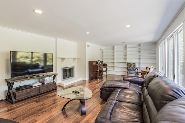 living room featuring recessed lighting, a glass covered fireplace, built in shelves, and wood finished floors