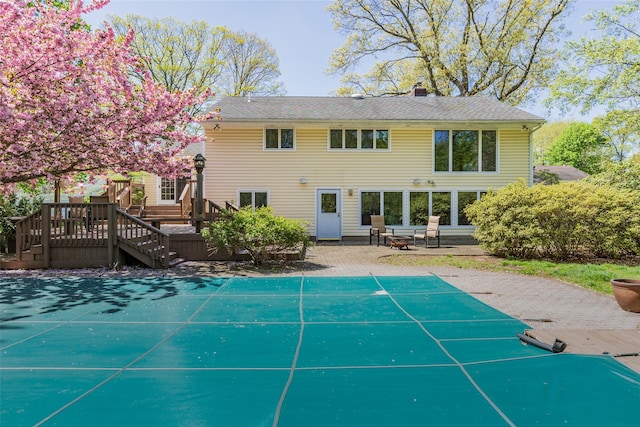 rear view of house with a chimney, a deck, stairway, a patio, and a covered pool