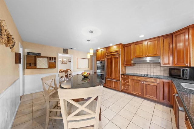 8 Richard Somers Rd, Granite Springs, NY 10527 - kitchen featuring light tile patterned floors, a wainscoted wall, brown cabinetry, under cabinet range hood, and appliances with stainless steel finishes