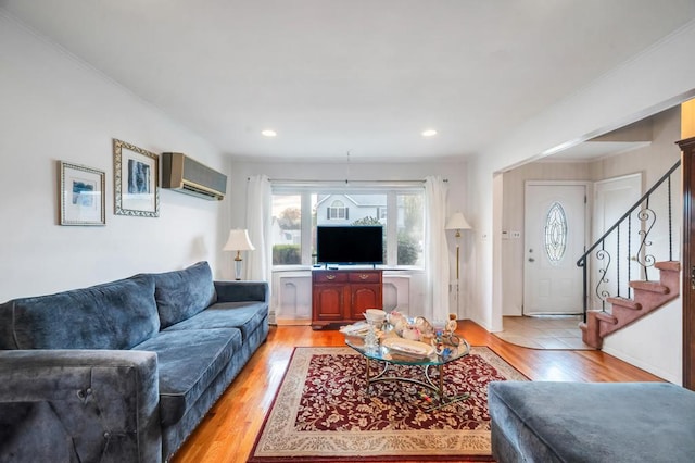 living area with stairway, light wood-type flooring, a wall unit AC, and ornamental molding